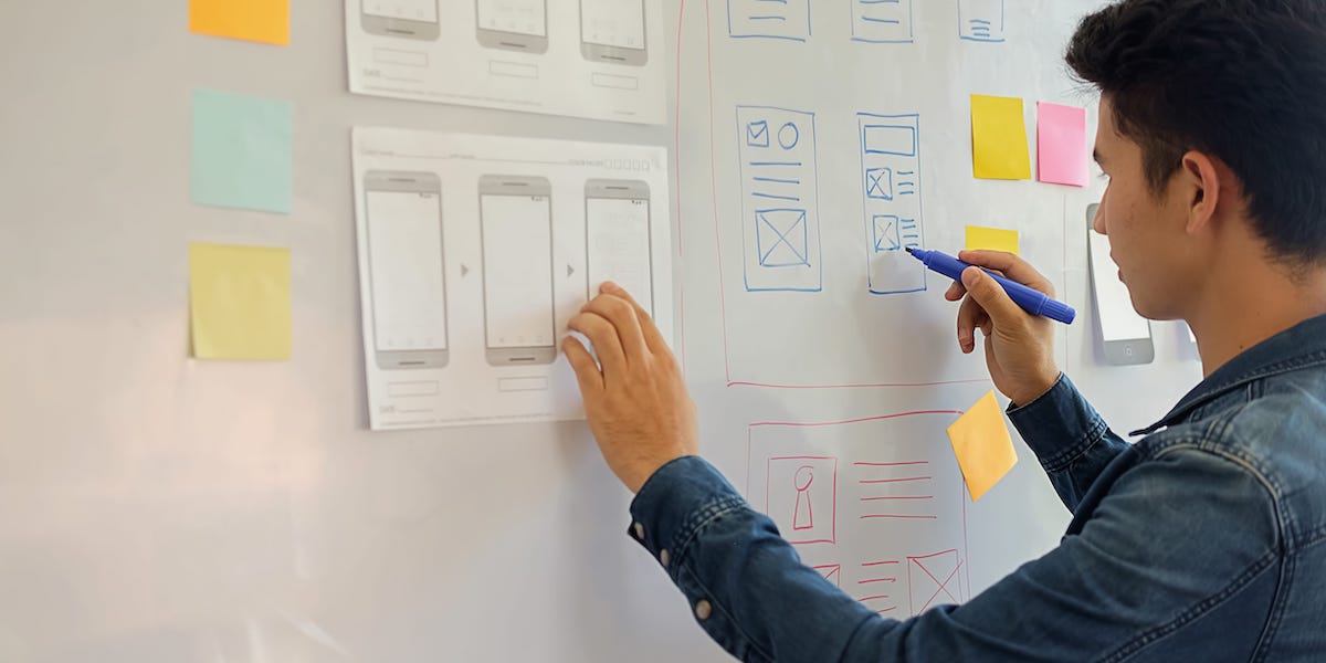 A UX designer uses the UX design process while transferring paper wireframes onto a whiteboard