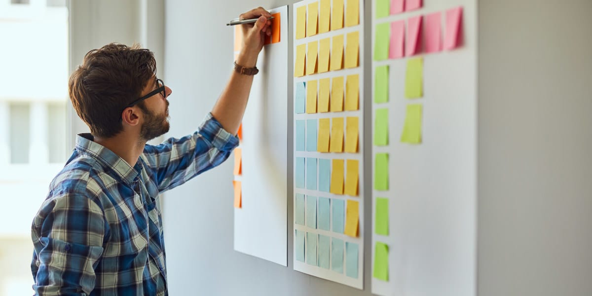 A designer standing at a whiteboard, writing ideas on sticky notes